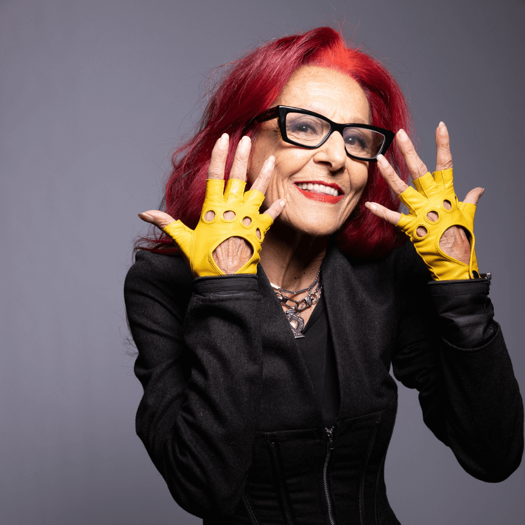 Designer Patricia Field modeling italian leather fingerless driving gloves from Emily in Paris featuring snap button closure.