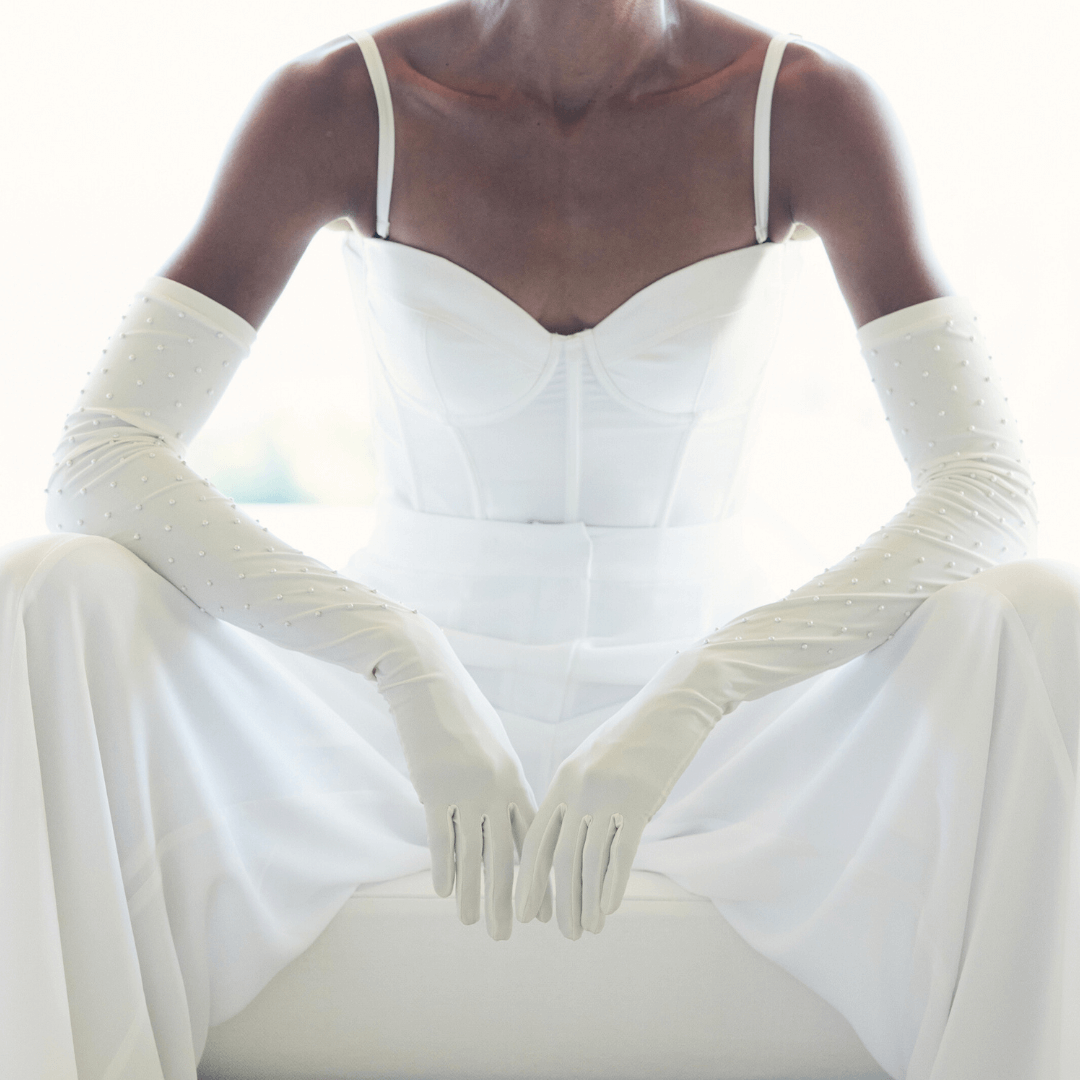 Close-up of a woman in all white wearing elegant white opera gloves embellished with delicate pearls.