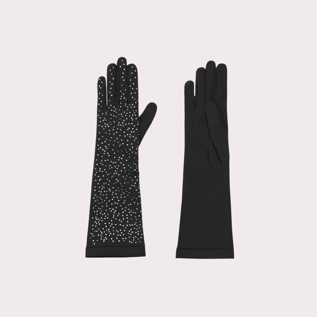 Flat lay of a pair of black opera gloves, one embellished with scattered crystals and the other plain, displayed on a light pink background.