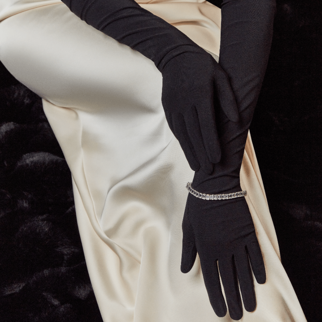 Elegant woman on a black velvet backdrop wearing a satin gown and black opera gloves with a subtle rhinestone detail.