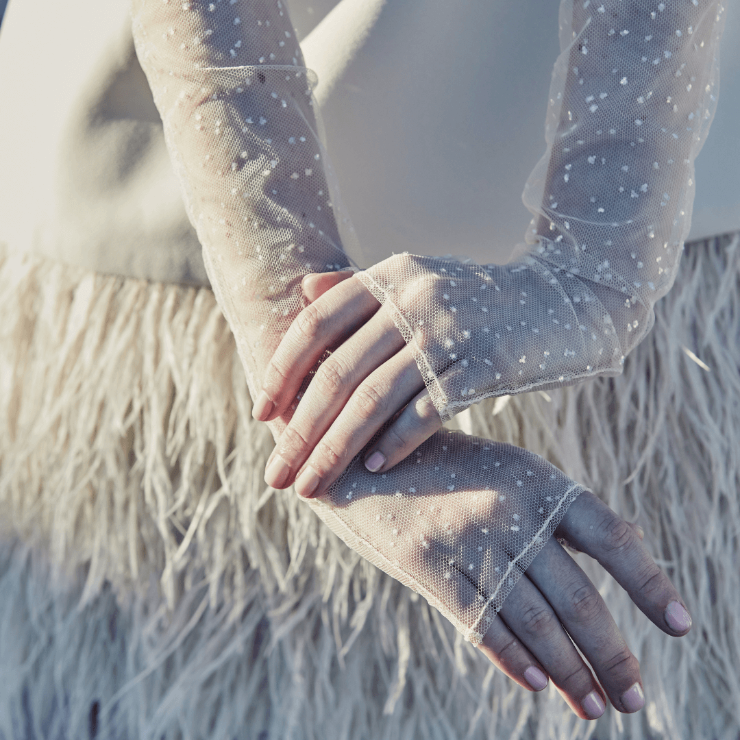 Close-up of sheer mesh opera gloves with details of glitter and finger loops, styled with an ivory feathered skirt in natural sunlight.