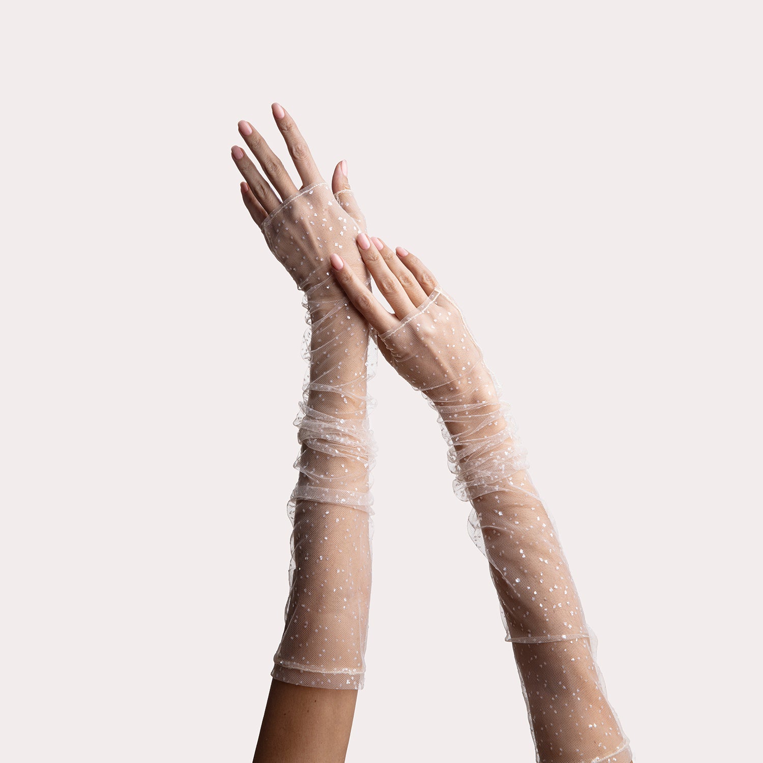 Close-up of arms wearing sheer mesh fingerless opera gloves with sparkling embellishments and finger loops, posed elegantly against a light background.