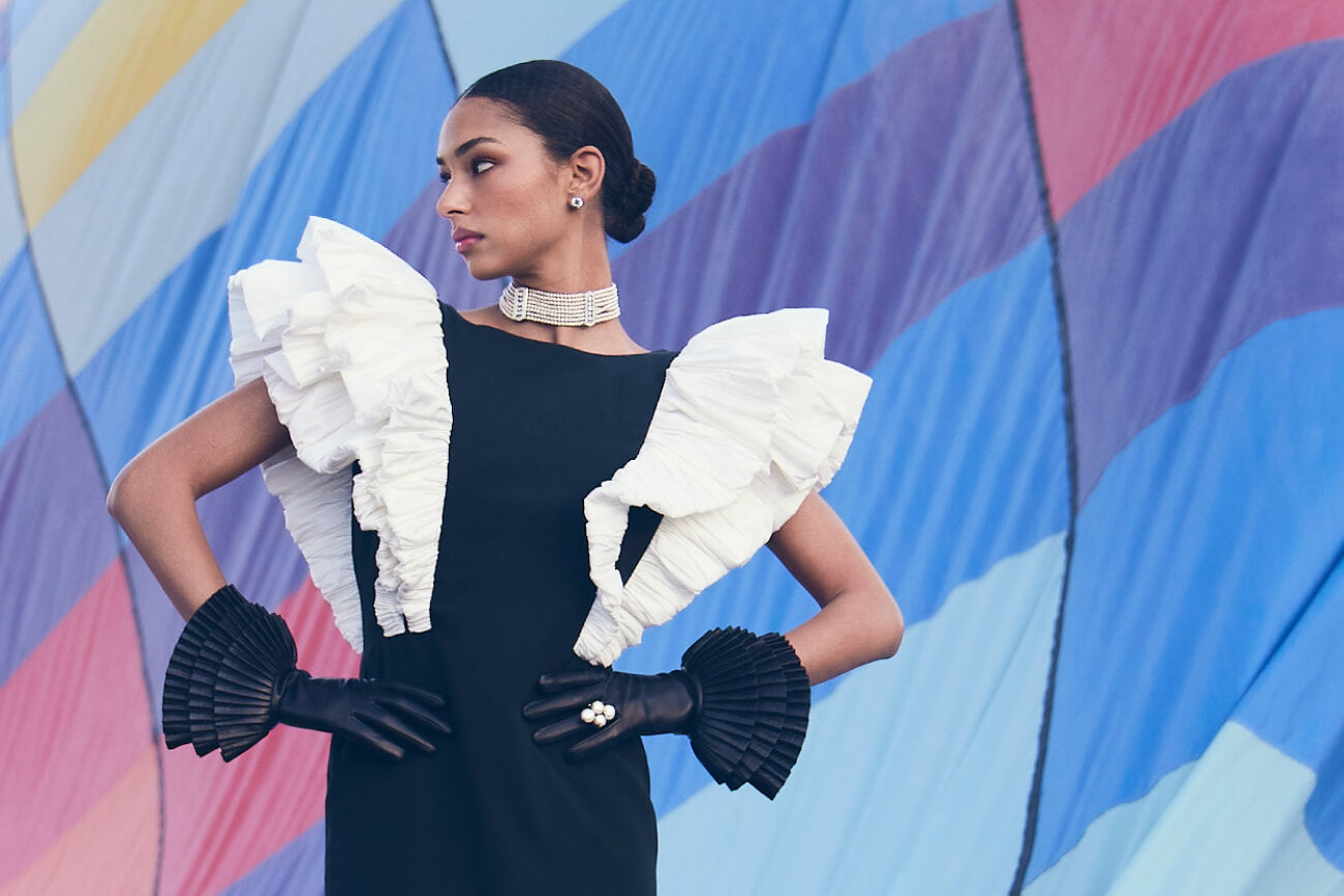 Black evening gown with dramatic white ruffles, pearl choker and pleated fans against colorful backdrop