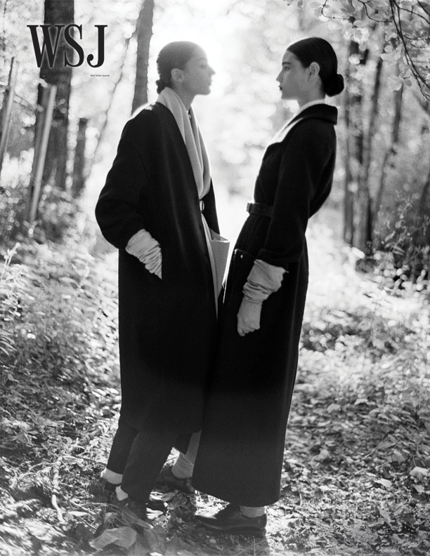 WSJ fashion editorial - Two models in black winter coats and white gloves facing each other in woodland setting, black and white photography