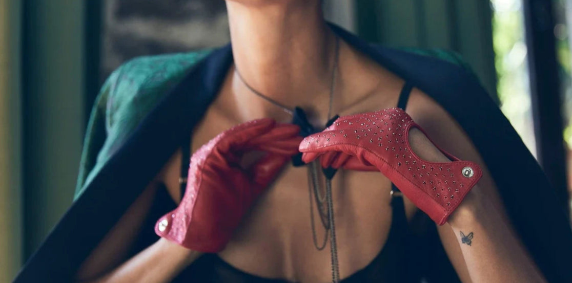 model tying necklace bow, jacket falling off shoulders, wearing red leather studded gloves