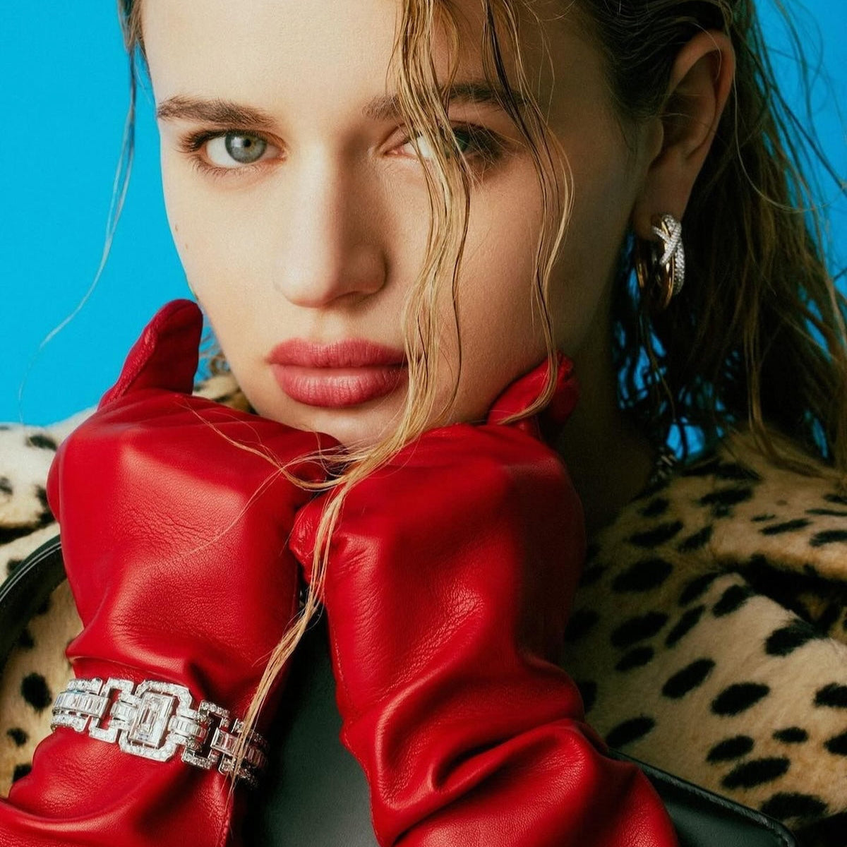 Red leather opera gloves with crystal bracelet detail against blue backdrop